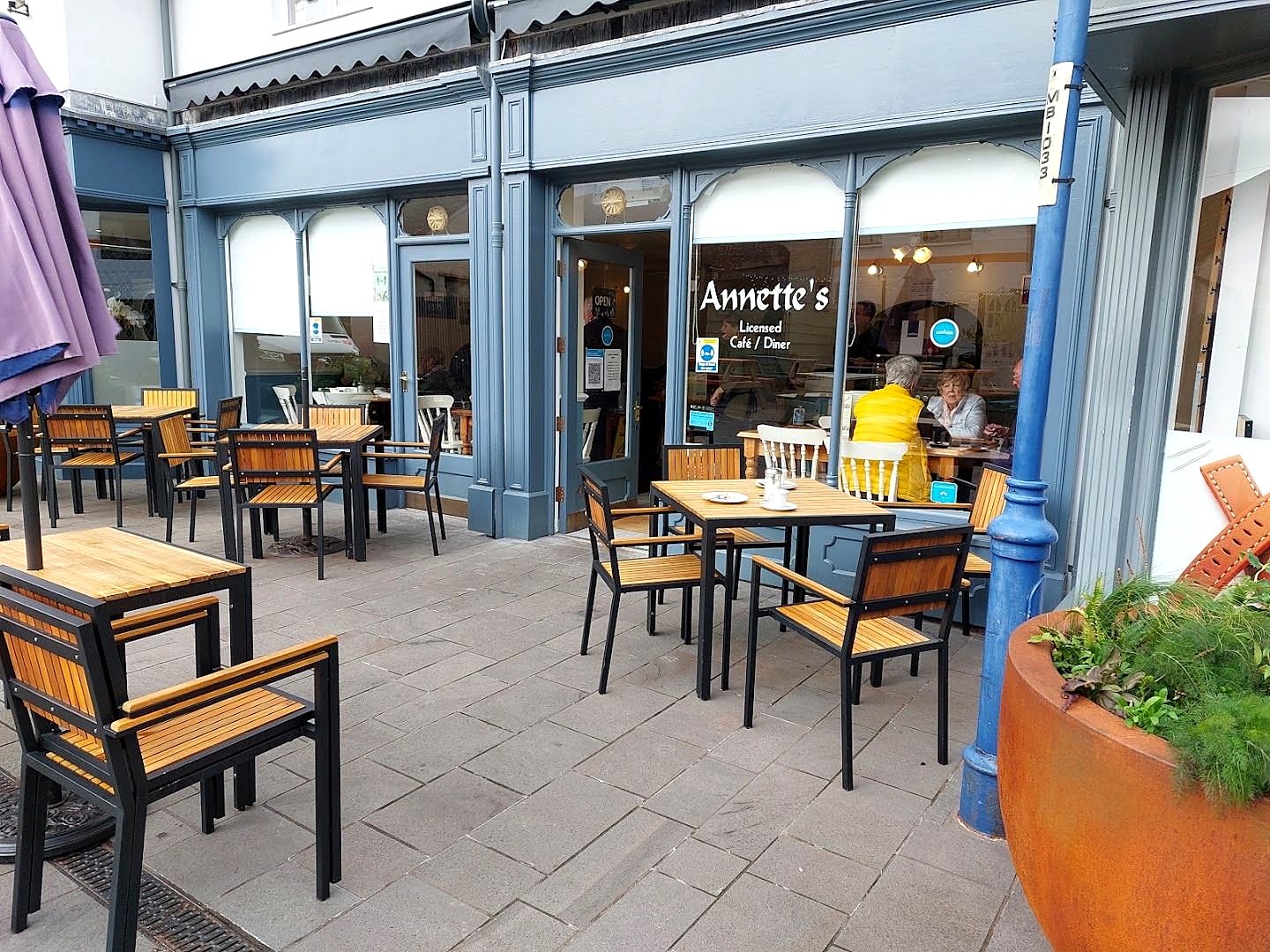 Annette's on Lewis Walk: a grey-blue shopfront with the name over the window, blue iron columns, and wooden tables and chairs set out on the paving