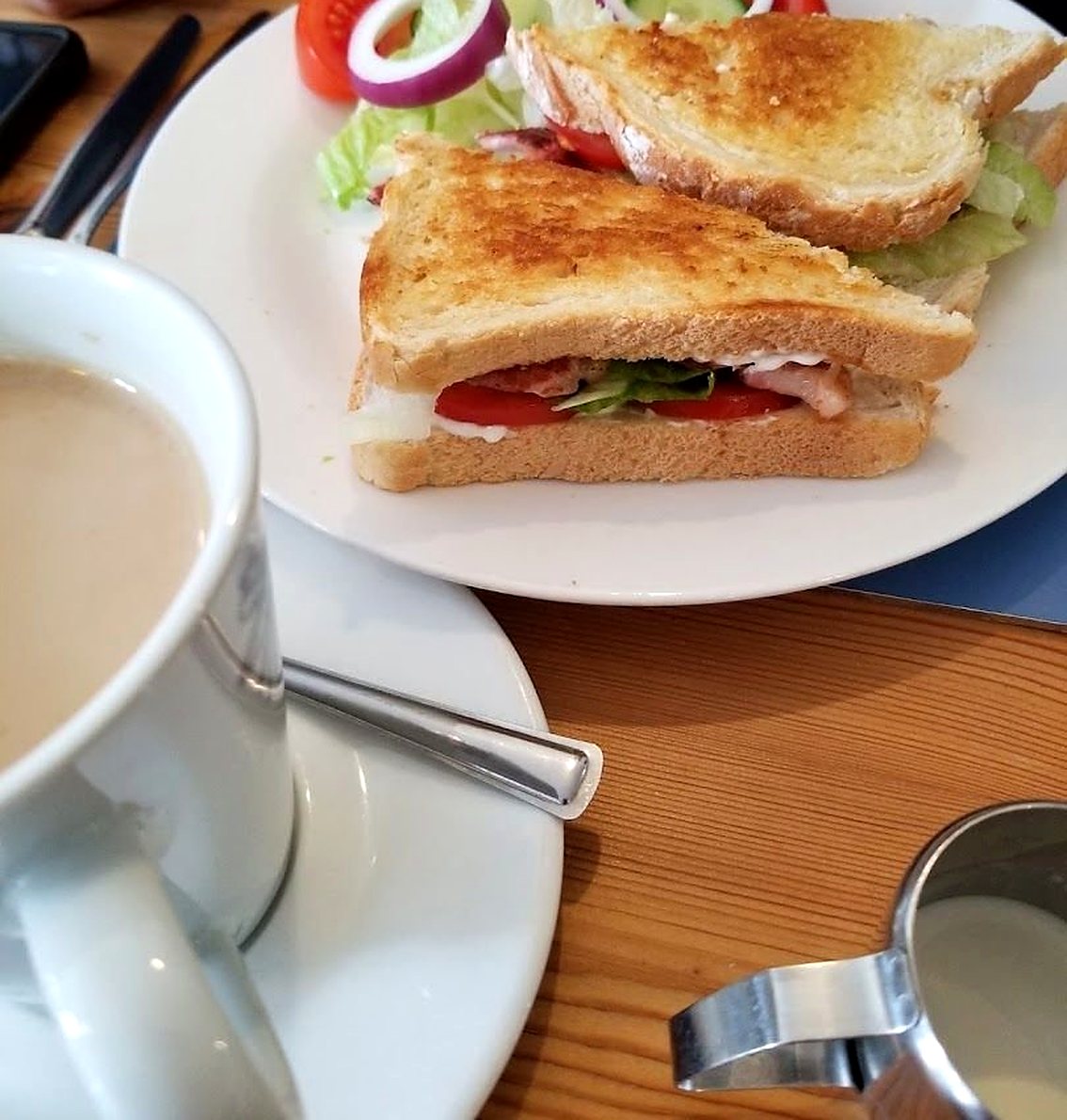 A toasted sandwich with salad on a white plate, next to a cup of tea and a small milk jug